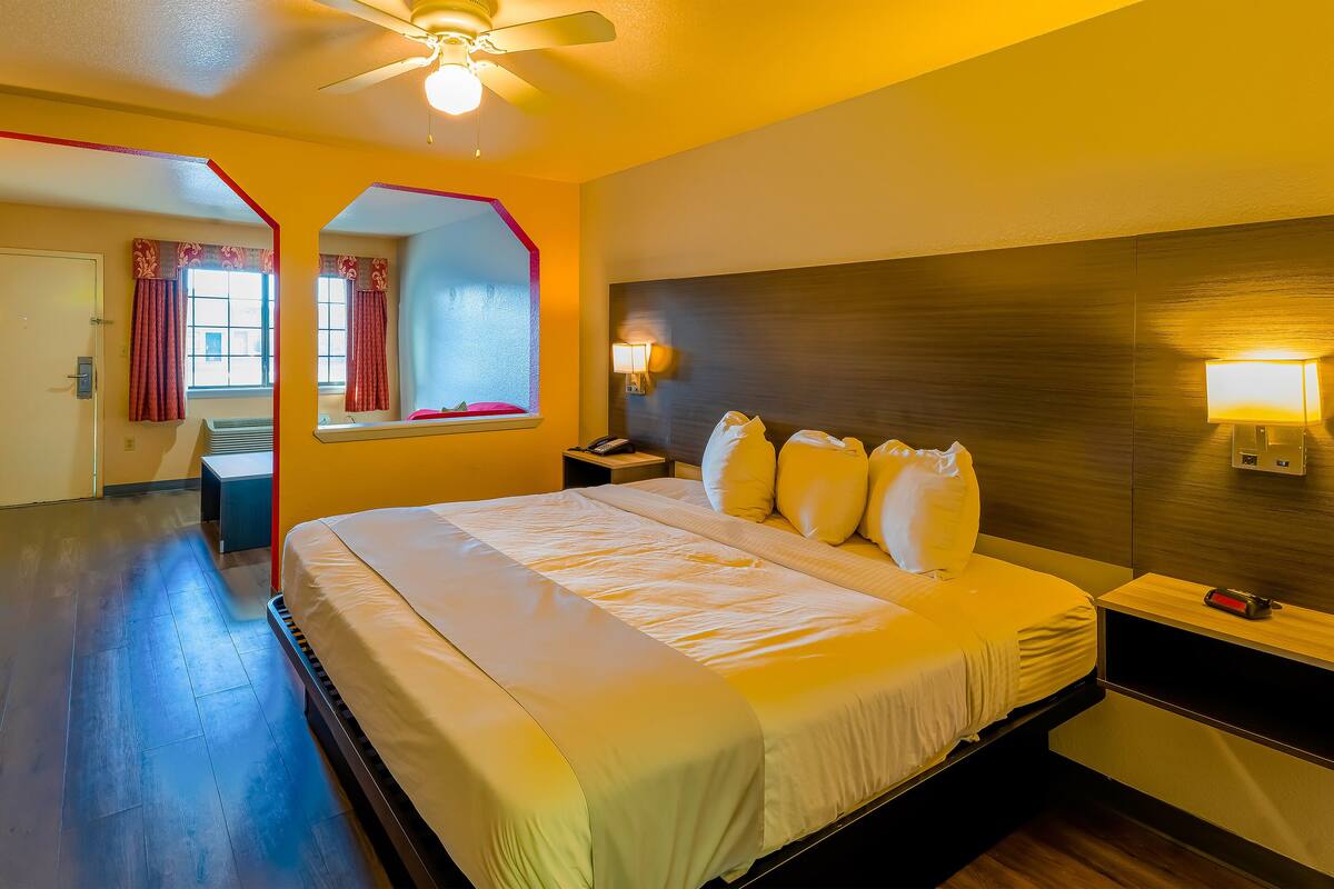 Une chambre d’hôtel comprenant un lit, des tables de chevet, une commode, un ventilateur de plafond et une fenêtre avec des rideaux.