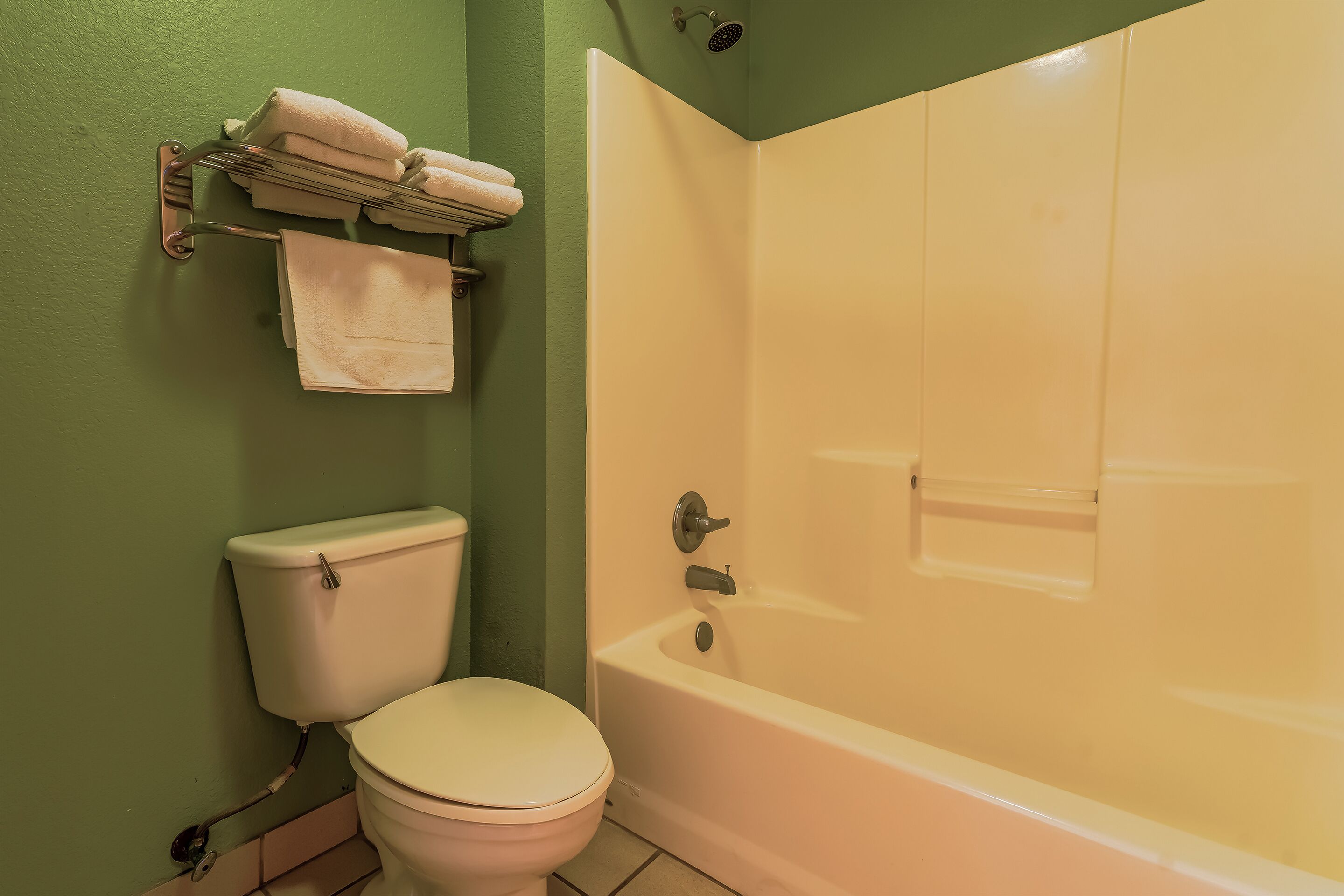 A bathroom with a toilet, a towel rack with towels, and a bathtub.