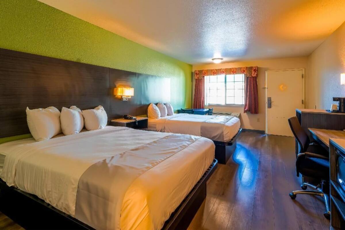 Une chambre d’hôtel avec deux lits, un bureau, une chaise et une fenêtre avec des rideaux.