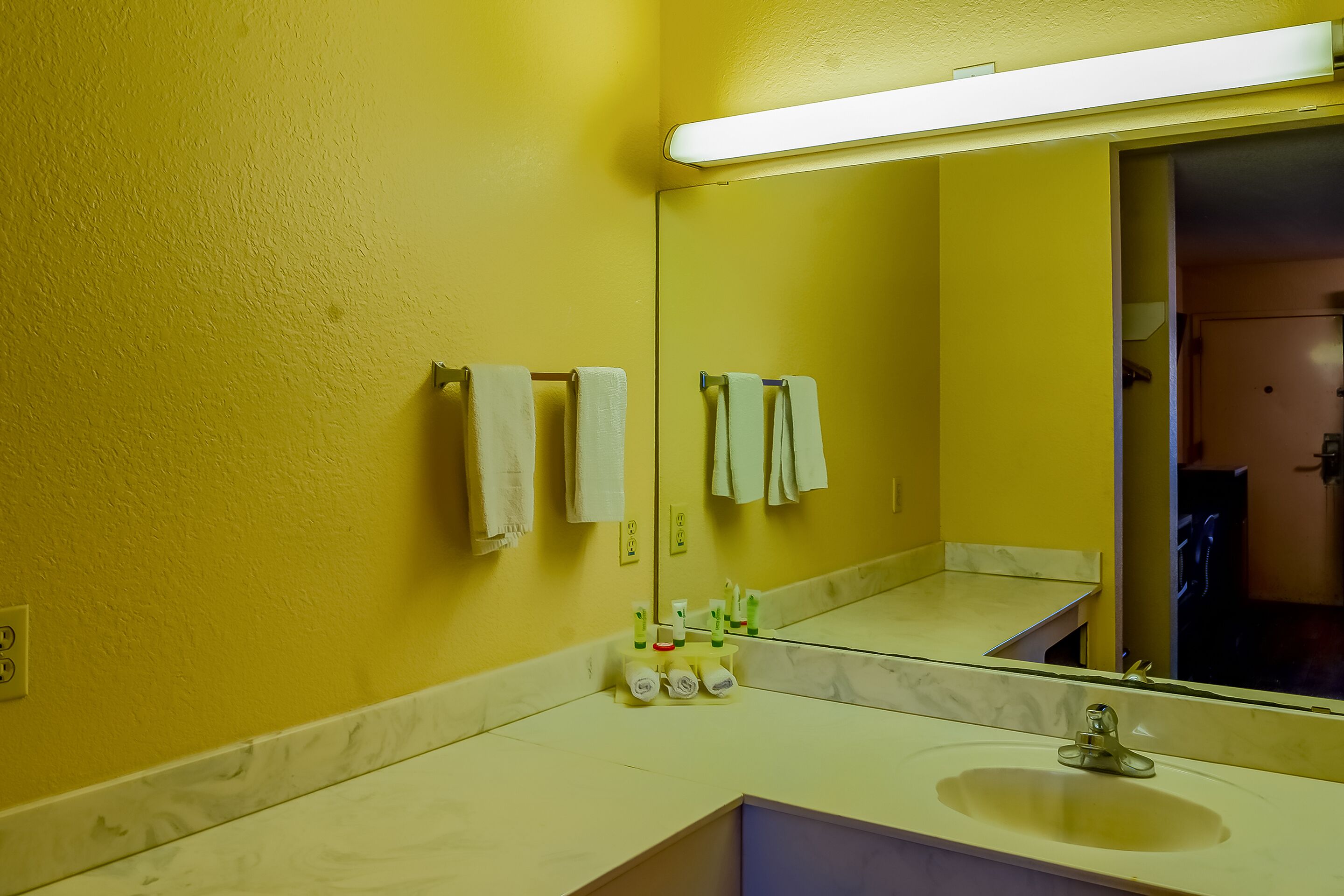 A bathroom with a yellow wall, a sink, a mirror, and towels hanging on the wall.