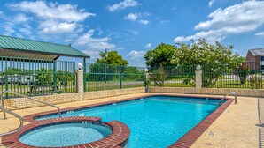 A rectangular swimming pool with a brick edge and a hot tub, surrounded by a green fence and a brick wall. - OYO Hotel Yoakum West (Yoakum)