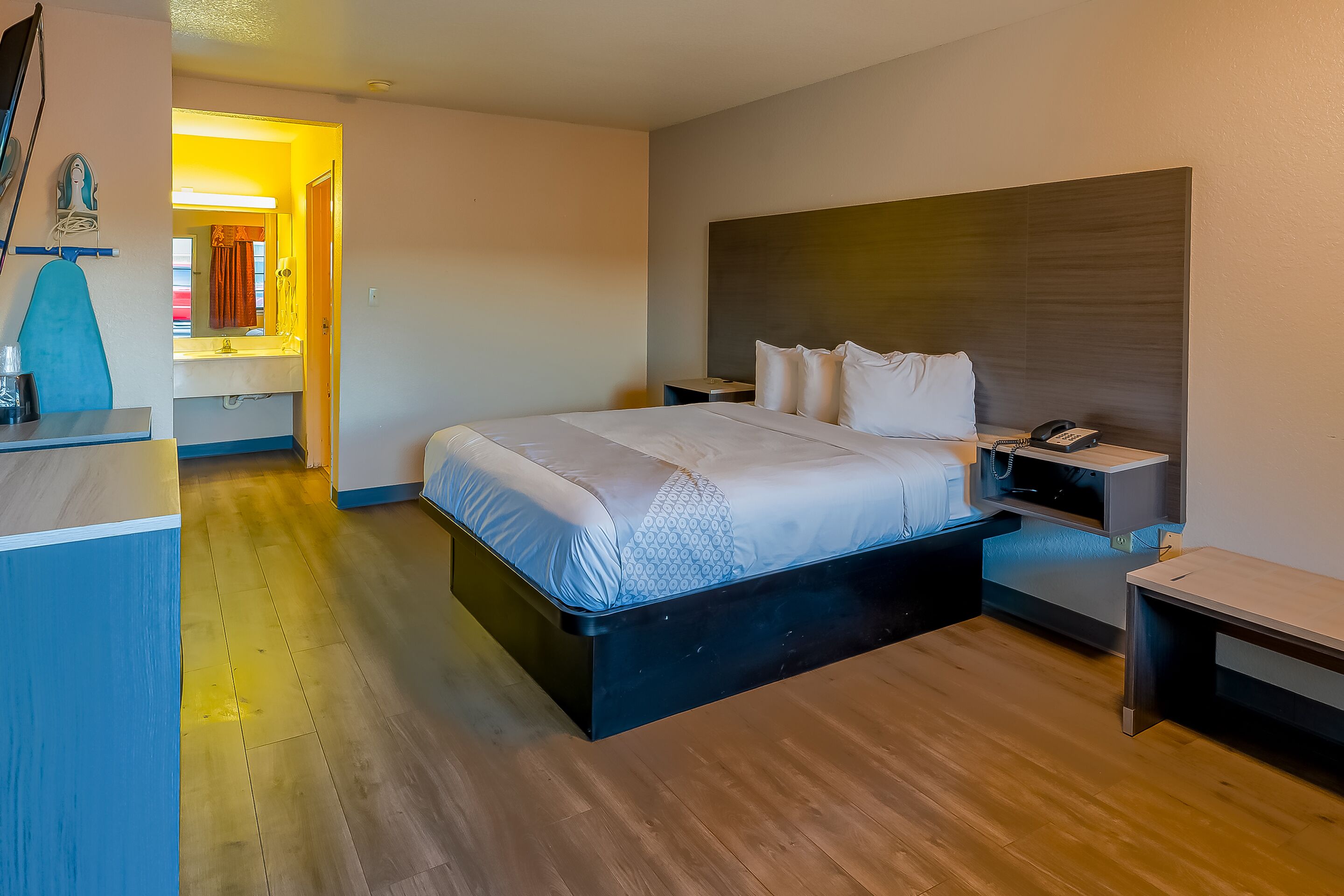 A modern hotel room with a large bed, bedside tables, a desk with a chair, and a bathroom visible through an open door.