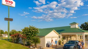 A hotel with a green roof, a signboard, and a parking area with a car and people. - OYO Hotel Yoakum West (Yoakum)