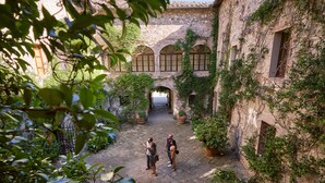 An outdoor courtyard with stone walls, arched windows, and potted plants. - Castello di Bossi (Castelnuovo Berardenga)