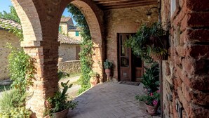 A covered outdoor area with brick arches, potted plants, and a door leading to a building. - Castello di Bossi (Castelnuovo Berardenga)