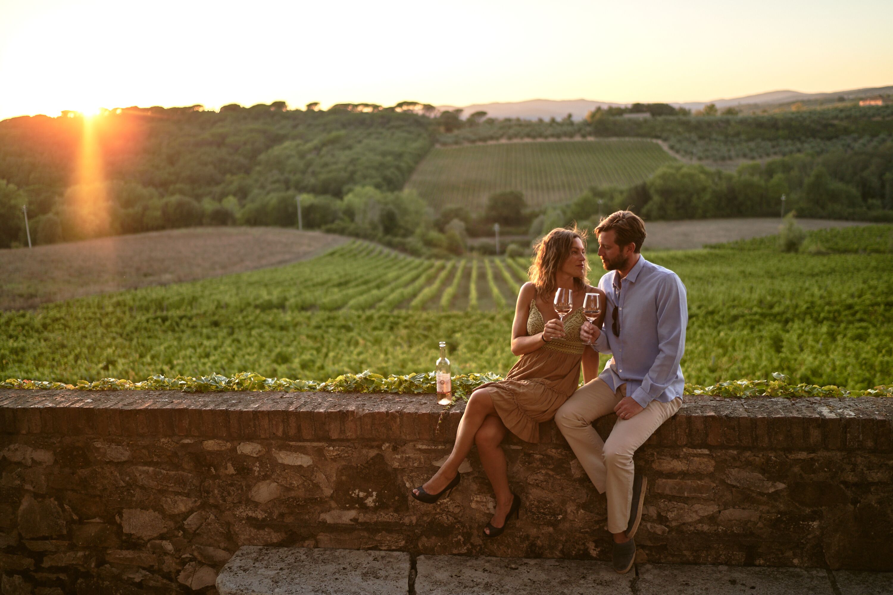 Ein Paar sitzt auf einer Steinmauer und blickt über einen Weinberg bei Sonnenuntergang.