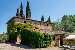 A rustic stone building with ivy-covered walls, a tiled roof, and a gravel courtyard.
