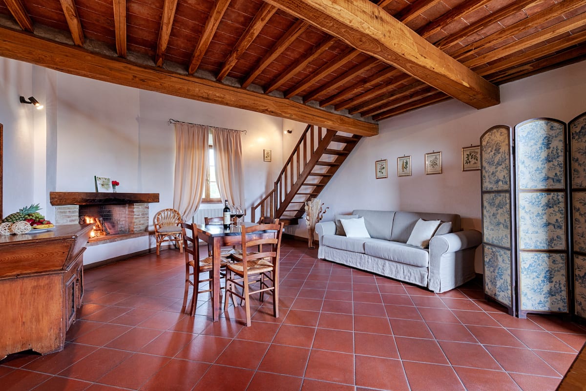 A rustic interior with a wooden ceiling, a dining area with chairs and a table, a sofa, and a fireplace.