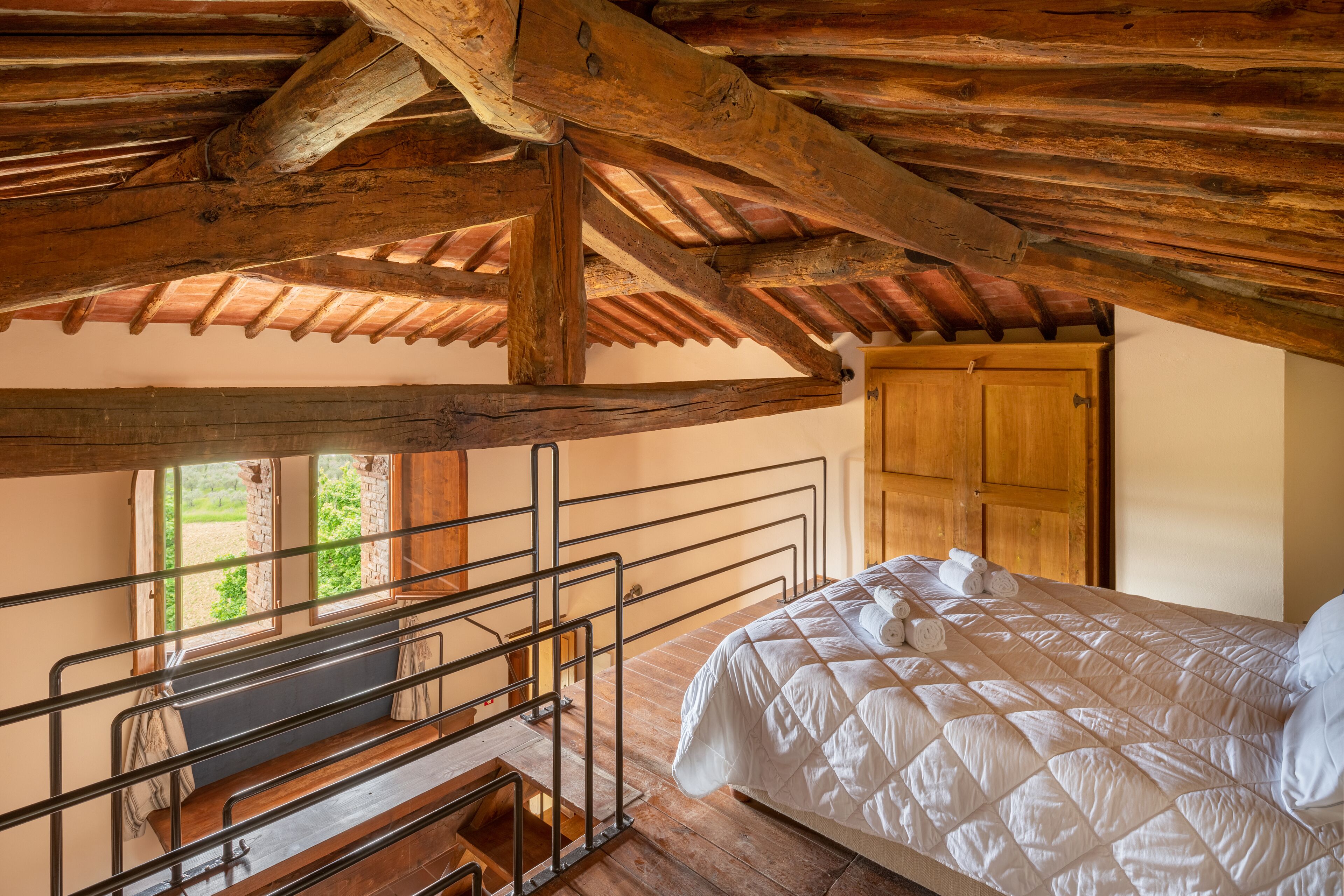 Un dormitorio con techo de madera, una cama con ropa de cama blanca, una puerta de madera y una ventana con vistas a la vegetación.