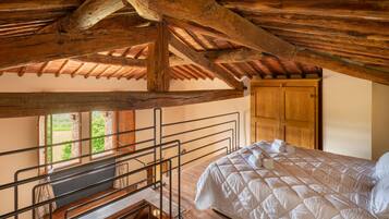 Un dormitorio con techo de madera, una cama con ropa de cama blanca, una puerta de madera y una ventana con vistas a la vegetación.