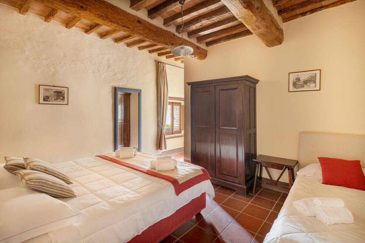 A bedroom with two beds, wooden beams on the ceiling, a wardrobe, and a small table.