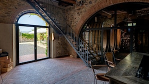A rustic interior with a stone wall, a wooden staircase, and a view of the outdoors. - Castello di Bossi (Castelnuovo Berardenga)