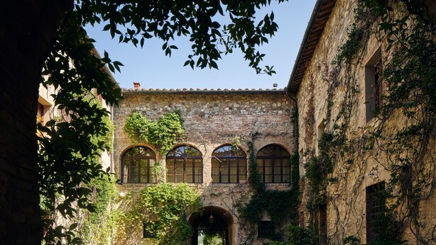 A courtyard with stone walls, arched windows, and potted plants. - Castello di Bossi (Castelnuovo Berardenga)