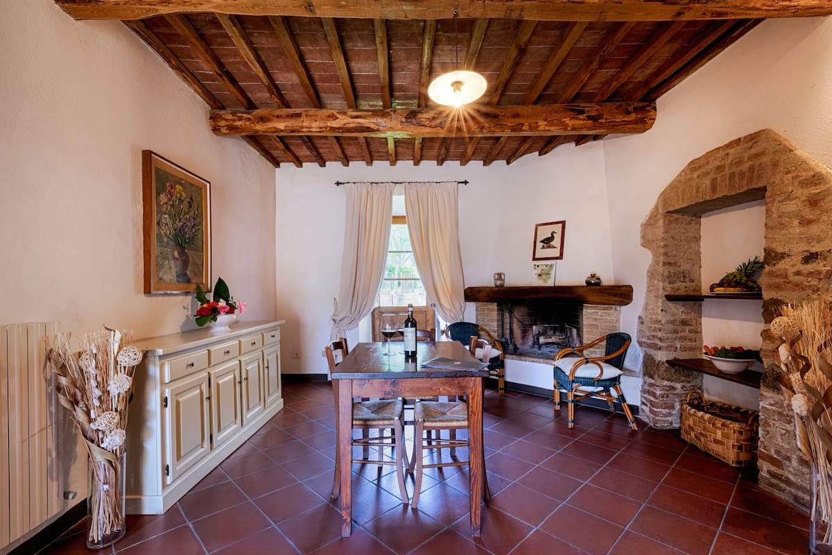 A rustic dining area with a wooden table and chairs, a fireplace, and a stone wall.