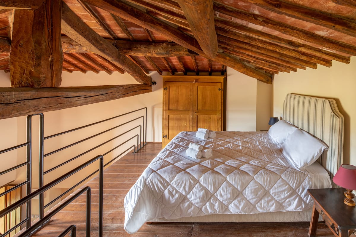 A bedroom with a wooden ceiling, a bed with a quilt, a nightstand, and a door in the background.