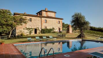 Un edificio de piedra con piscina, mobiliario exterior y un césped bien cuidado.