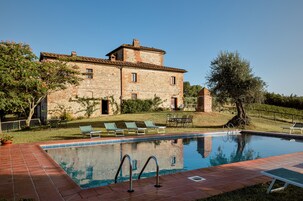 A stone building with a swimming pool, outdoor seating, and a well-maintained lawn.
