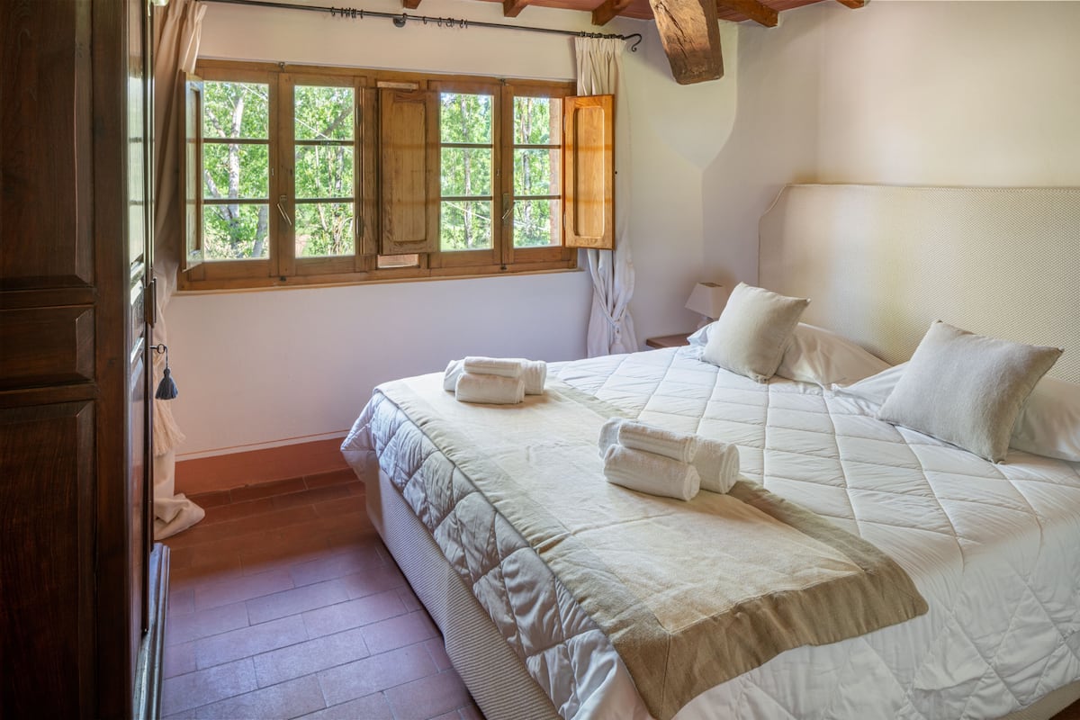 A bedroom with a large bed, a window with wooden shutters, and a wooden ceiling beam.