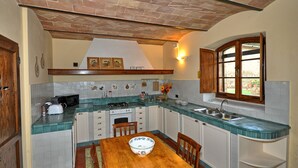 Cozinha com mesa de madeira, armários brancos e janela.