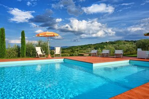 A swimming pool with lounge chairs and an umbrella, surrounded by greenery and hills. - Villa Rachele (Casole d'Elsa)