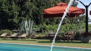 Una piscina con agua que cae, rodeada de sillas de descanso y una sombrilla.
