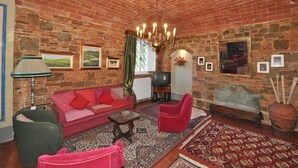 Una sala de estar acogedora con techo de ladrillo, un sofá rojo, un sillón verde, una mesa de centro de madera y una alfombra estampada.