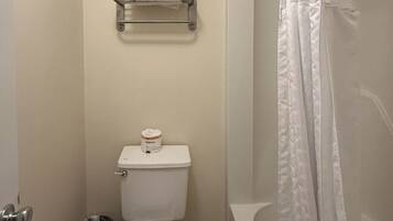 Een badkamer met een toilet, een plank met handdoeken, een prullenbak en een douchegordijn.