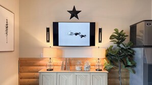 A modern living room with a wooden bench, a TV mounted on the wall, a star decoration, and a refrigerator. - The Trail Inn - Grantsburg (Grantsburg)