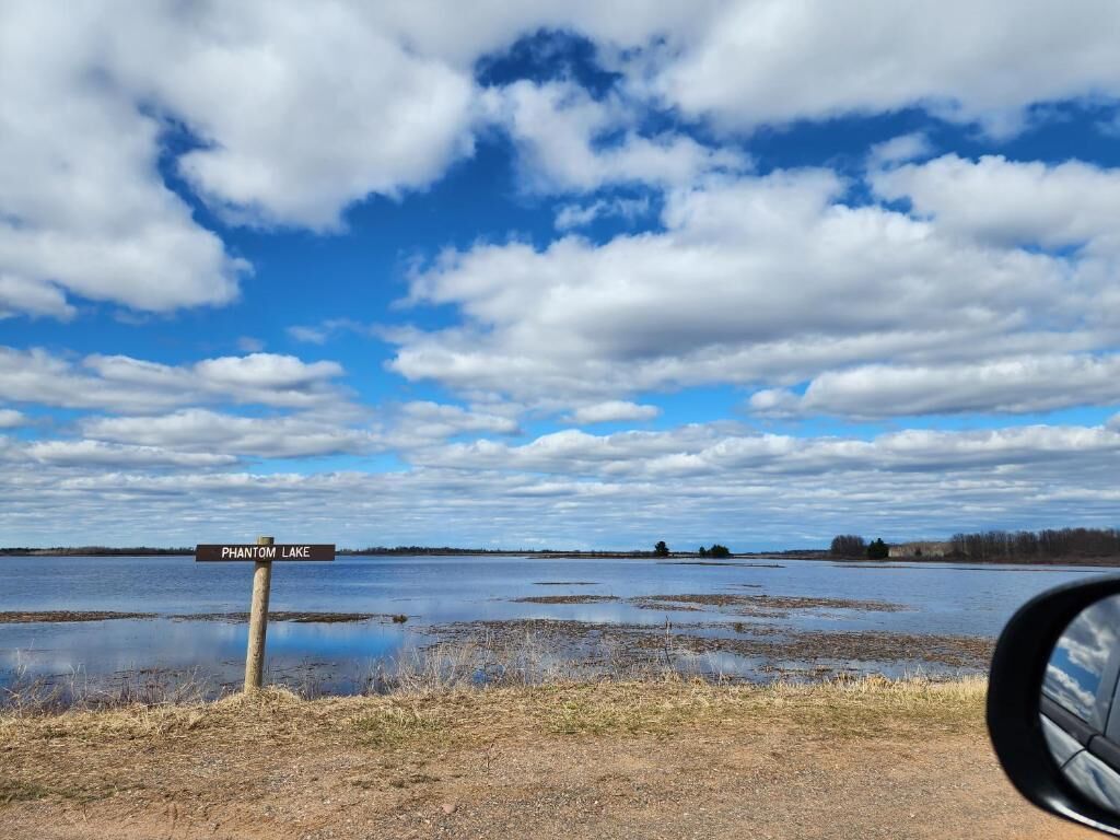 A signpost with 'PHANTOM LAKE' written on it, a body of water, and a clear sky with clouds.