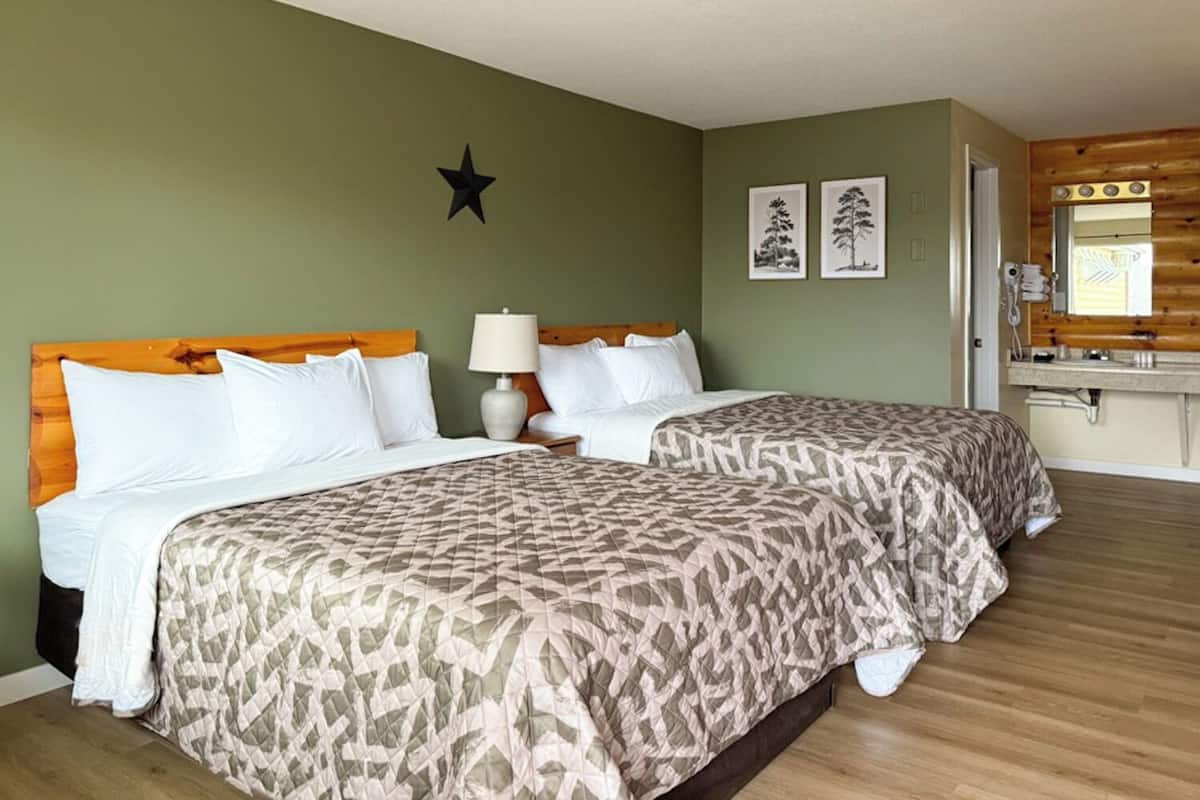 A double room with two beds, a wooden headboard, a bedside lamp, and a small mirror above the sink.