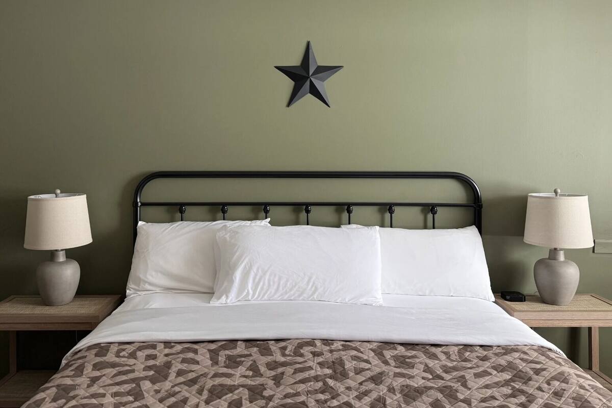 A neatly made bed with white linens and a patterned duvet, flanked by two bedside tables with lamps and a star decoration on the wall.