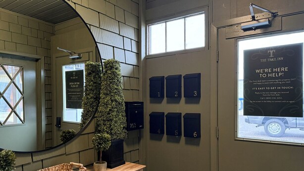 A reception area with a wooden desk, a mirror, numbered mailboxes, and a welcome sign. - The Trail Inn - Grantsburg (Grantsburg)