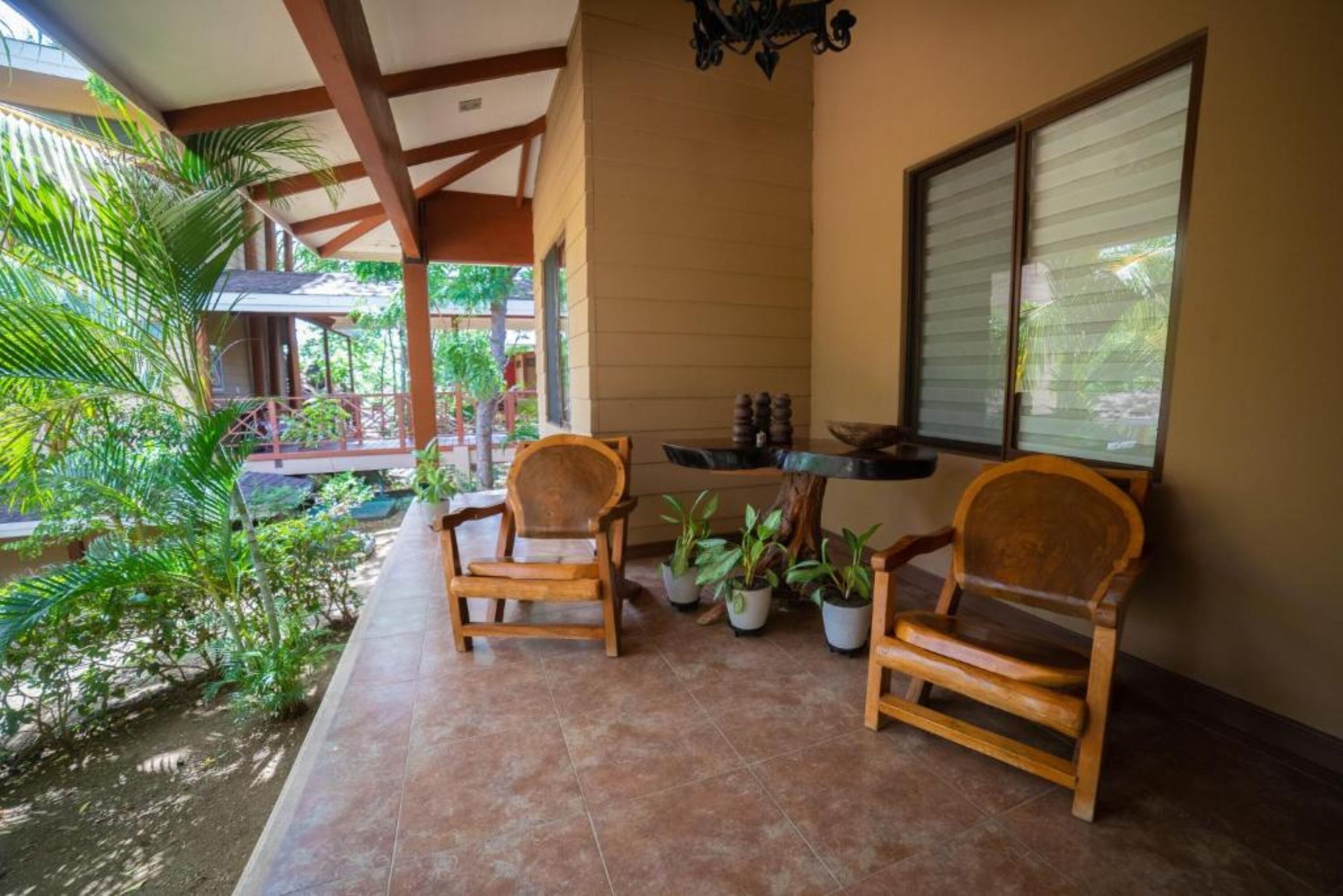 A covered patio with two wooden chairs, potted plants, and a window with blinds.