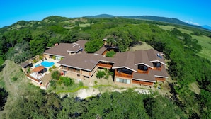 Um resort grande e moderno com vários edifícios, piscina e vegetação exuberante ao redor.