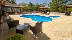 Um quintal com piscina, cadeiras de descanso e um gazebo.