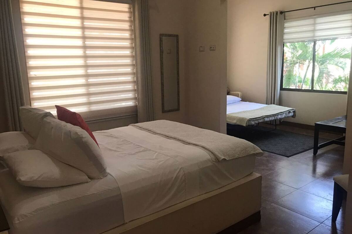 A hotel room with a large bed, a smaller bed, a desk, and a window with blinds.