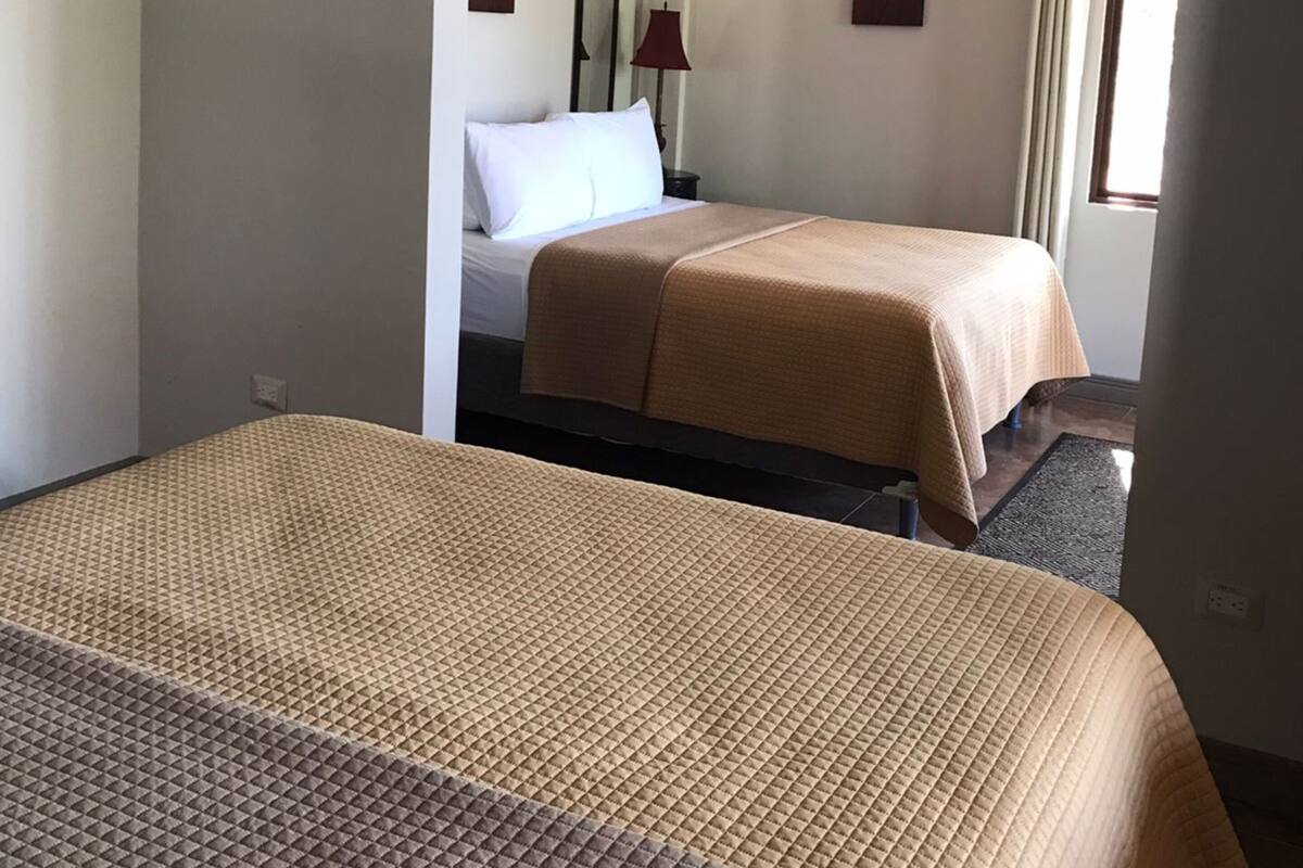 A hotel room with two beds, a nightstand, a lamp, and two wall-mounted paintings.