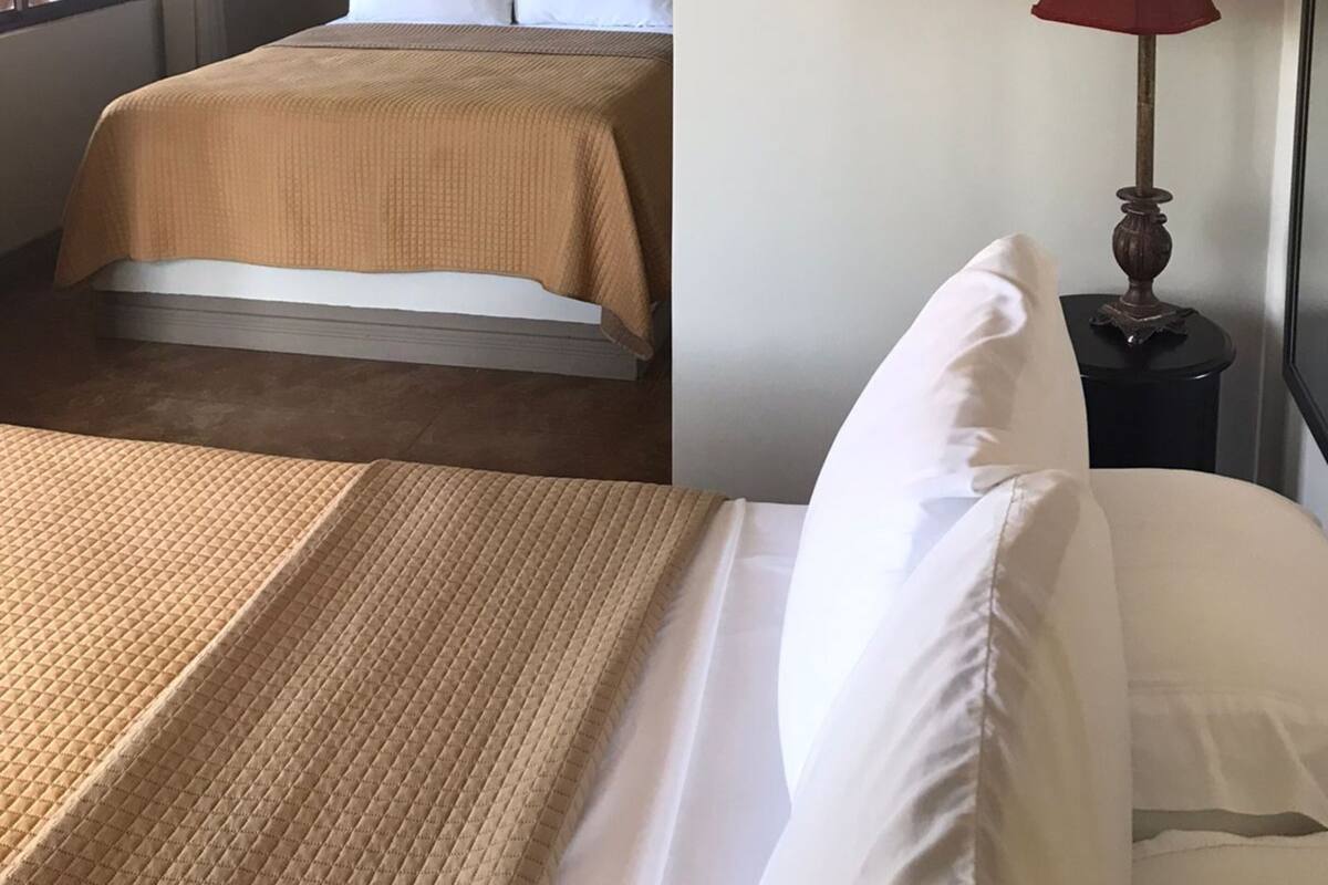 A hotel room with two beds, a brown headboard, a red lamp, and a window with blinds.