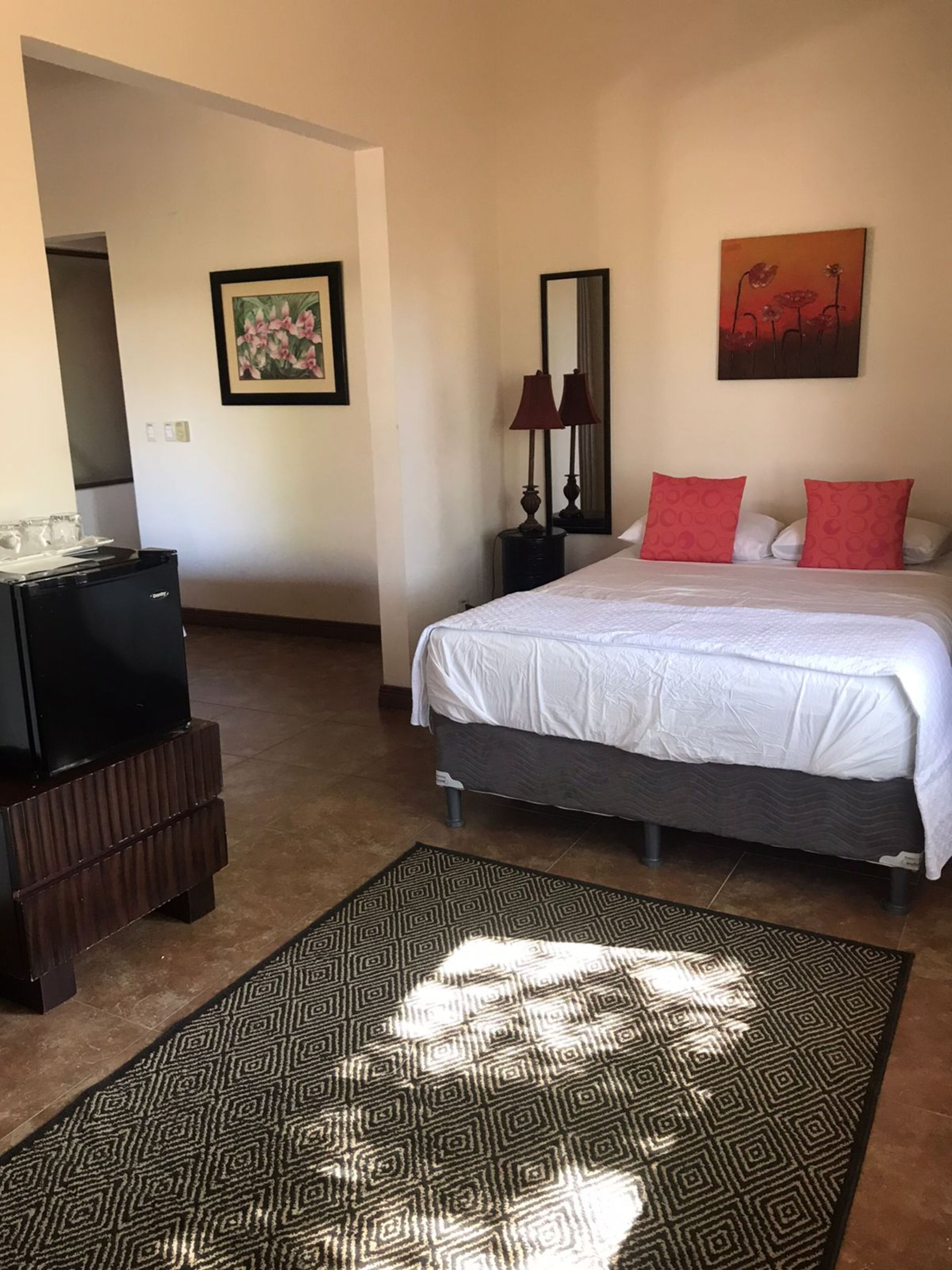 Een hotelkamer met een bed, een bureau, een spiegel en een schilderij aan de muur.