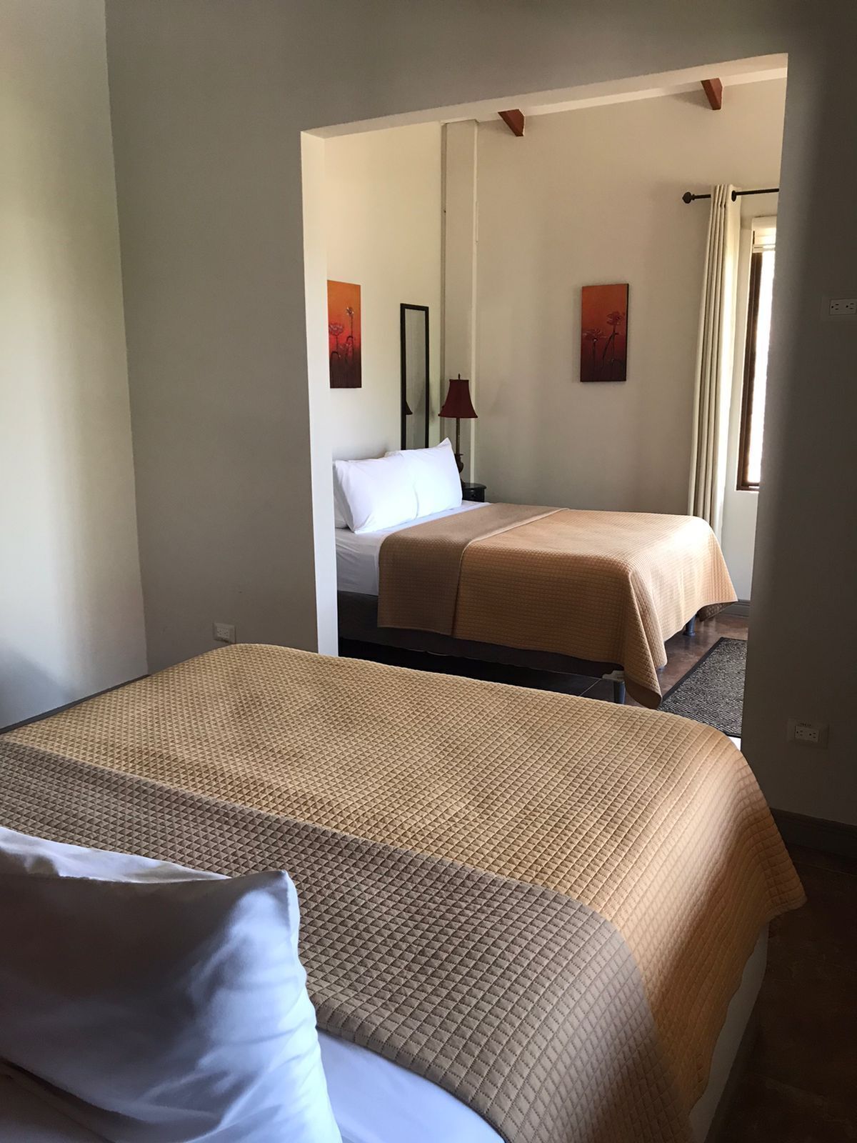 Hotellihuone, jossa on kaksi sänkyä, ikkuna, jossa on verhot, ja taideteoksia seinillä.