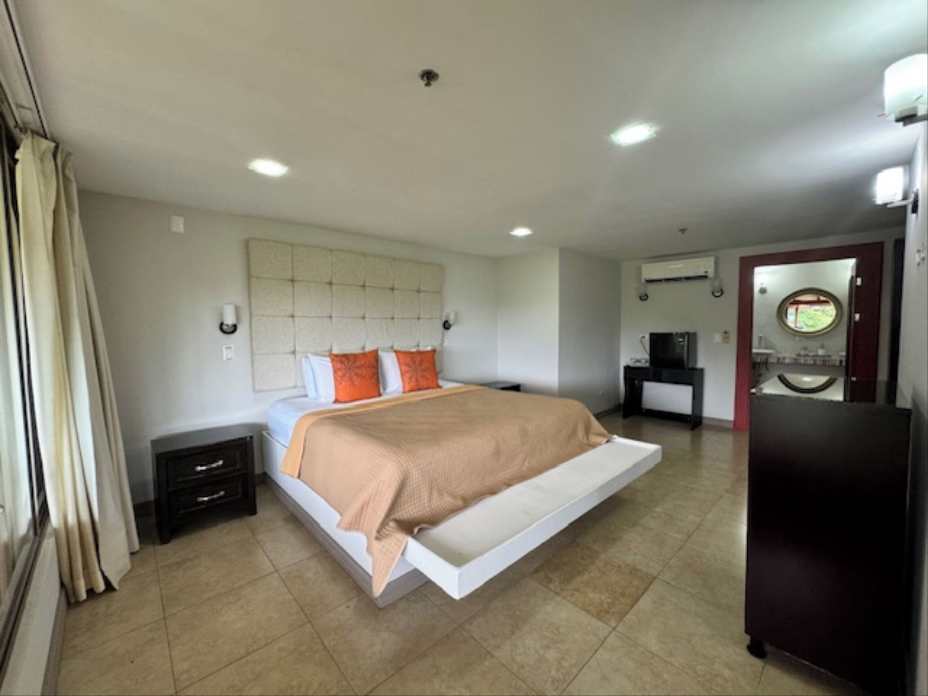 A modern hotel room with a large bed, a flat-screen TV, a desk, and a bathroom with a mirror and sink.