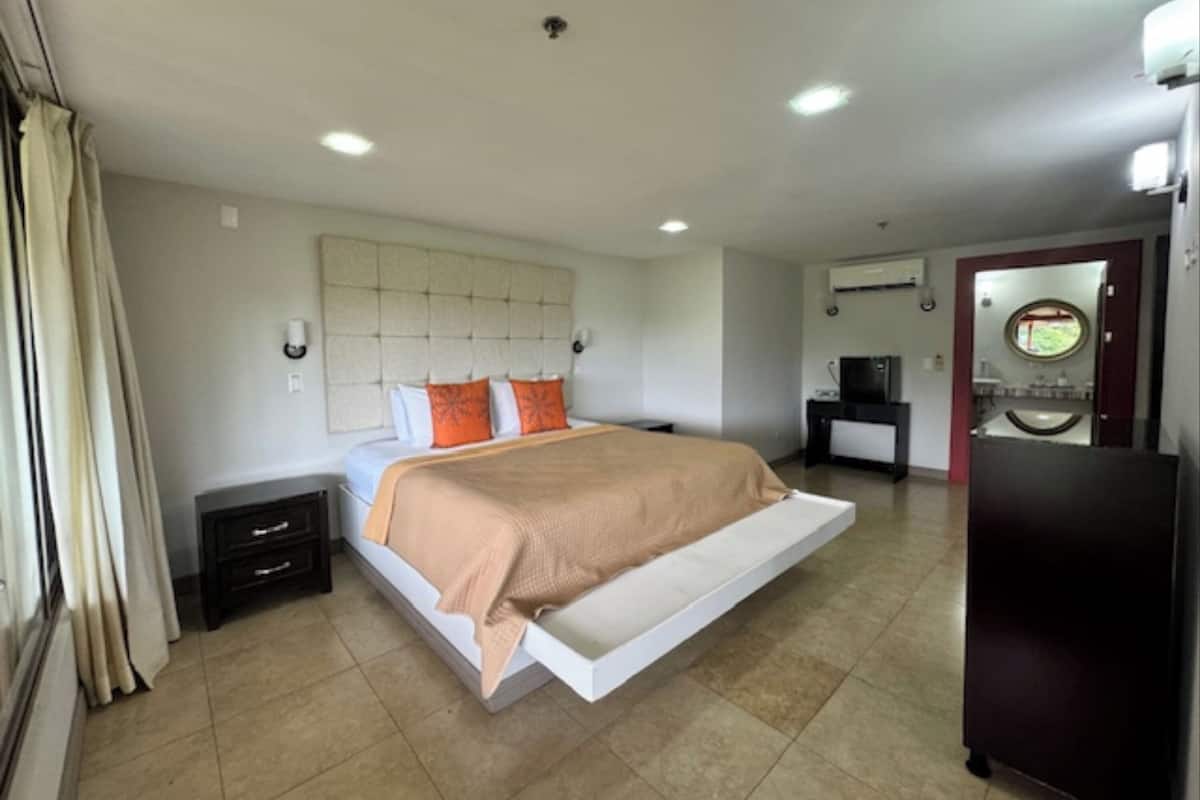 A modern hotel room with a large bed, a flat-screen TV, a desk, and a bathroom with a mirror and sink.