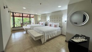 Quarto de hotel com duas camas, um banquinho, um espelho redondo e uma mesinha com copos.