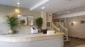 A reception desk with a mirror, potted plants, and a staircase leading to another level. - Hotel Arcea Villaviciosa (Villaviciosa)