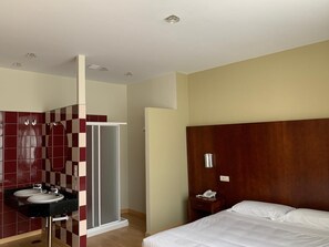 A hotel room with a wooden headboard, a bed with white linens, a bathroom with a checkered tile wall, a sink, and a shower. - Hotel Arcea Villaviciosa (Villaviciosa)