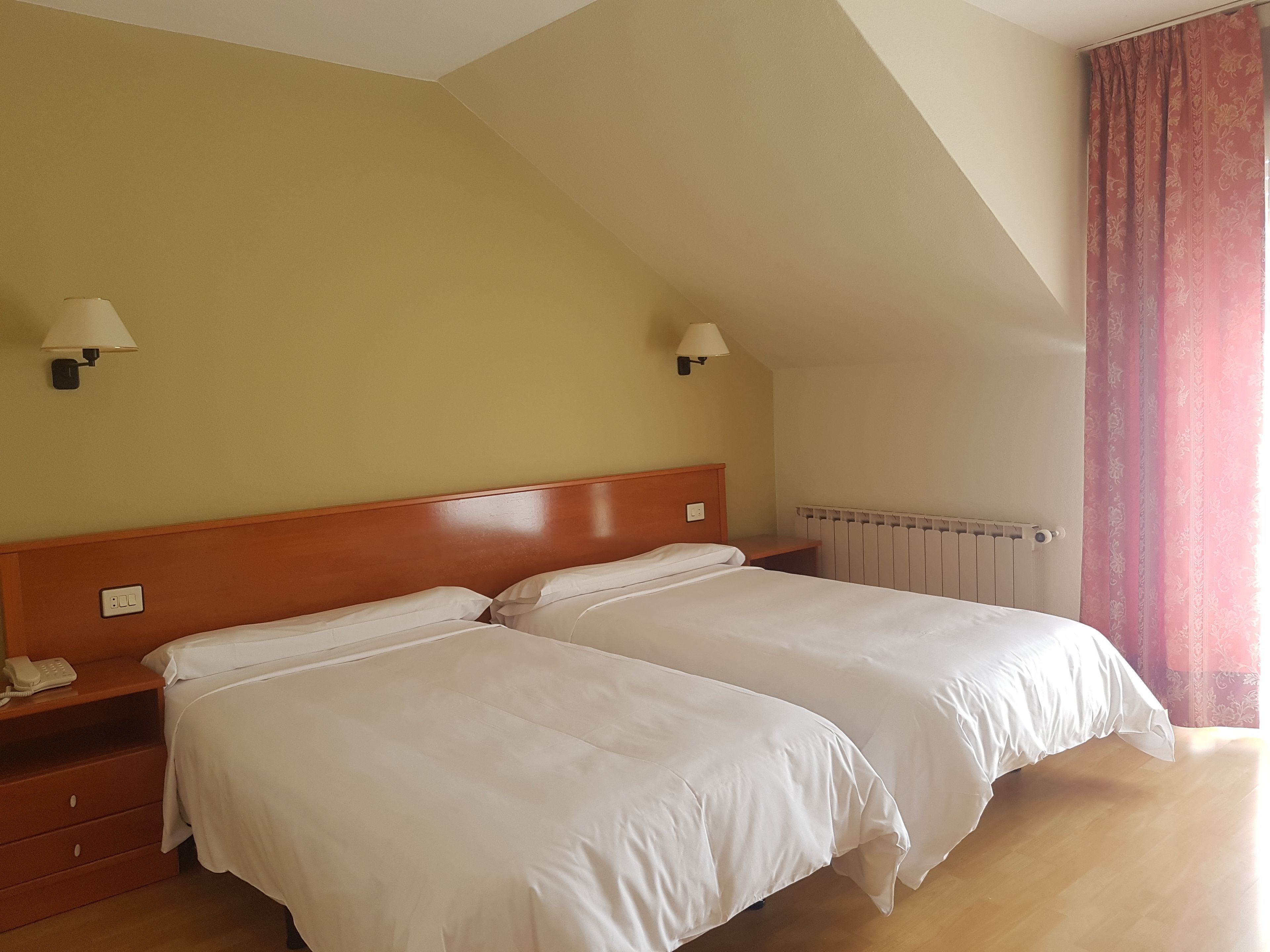 A hotel room with two beds, a wooden headboard, bedside lamps, a telephone, and a radiator.
