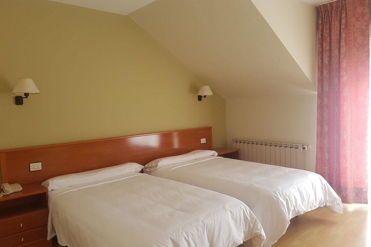 A hotel room with two beds, a wooden headboard, bedside lamps, a telephone, and a radiator.