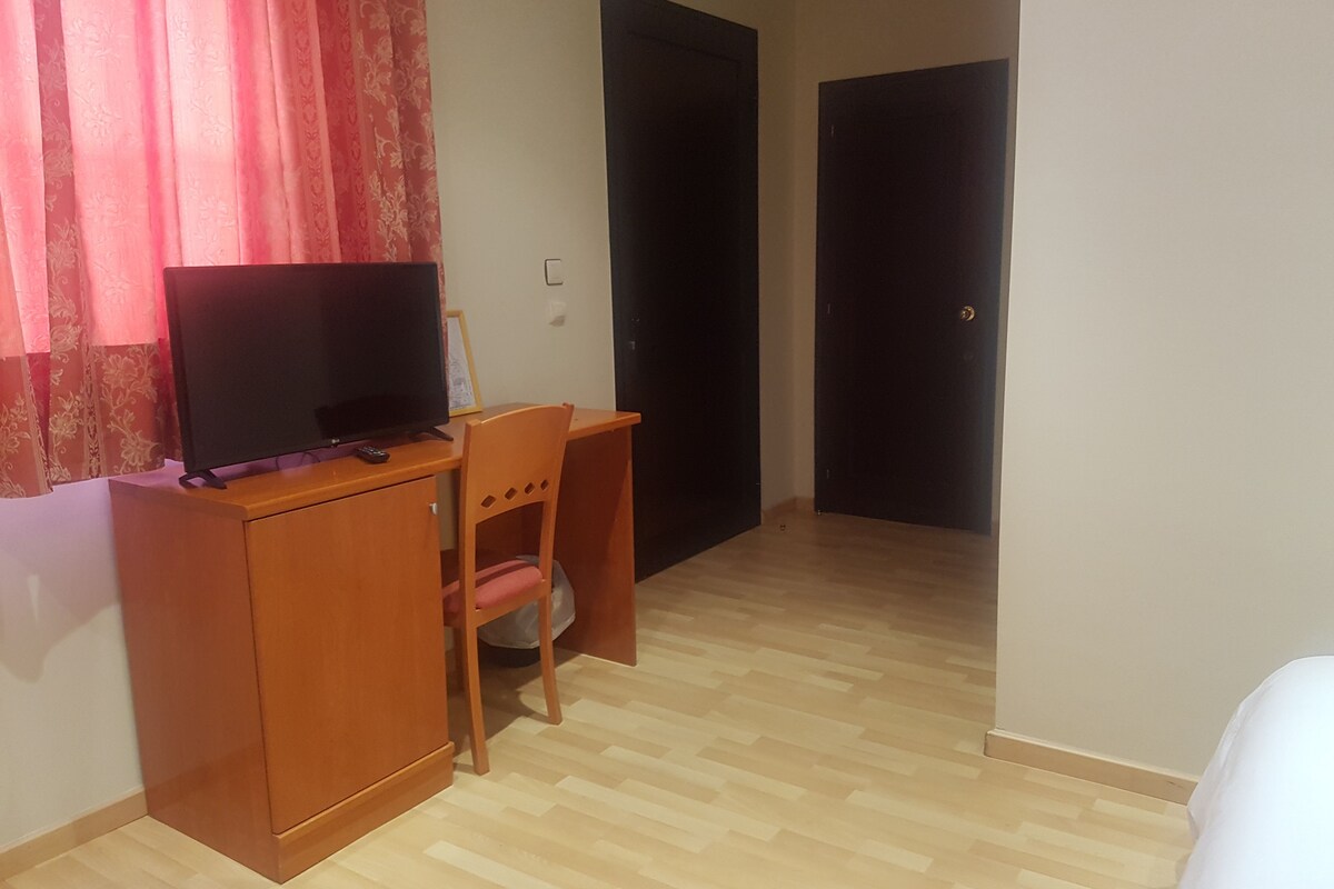 A room with a wooden desk, a chair, a television, and two doors.