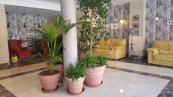 Un vestíbulo con piso de mármol, un sillón rojo, sofás amarillos y plantas en macetas.