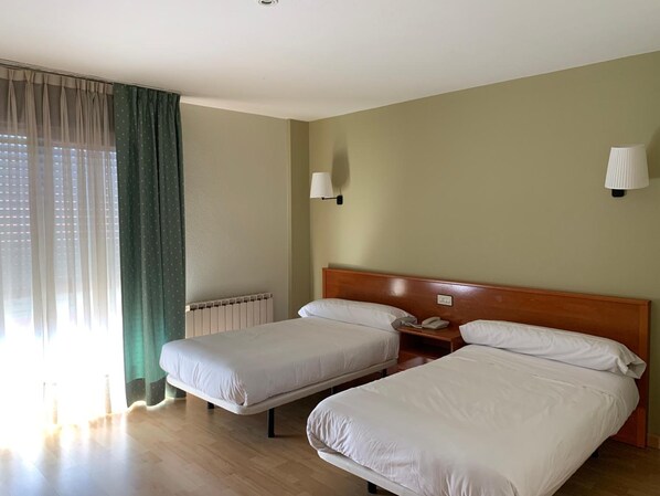 A hotel room with two single beds, a wooden headboard, a bedside table with a lamp, and a window with sheer curtains. - Hotel Arcea Villaviciosa (Villaviciosa)